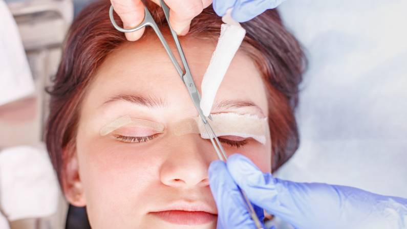 Female surgeon applies a bandage to the female patient's eyelids after a blepharoplasty operation.