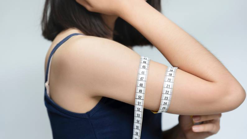 A beautiful woman raises her arms to measure her arm circumference with a white tape measure