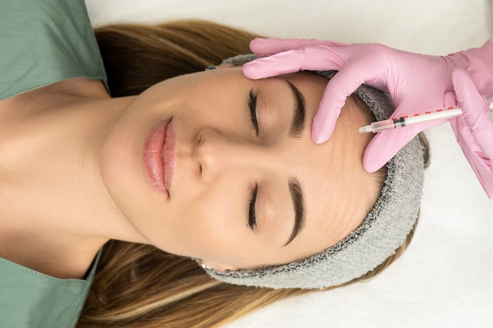 Close-up of the hands of an expert cosmetologist injecting botox into a woman's forehead.